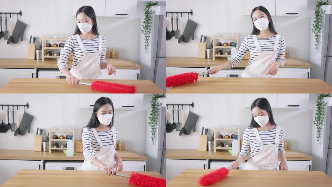 年轻快乐的亚洲妇女打扫家，戴着口罩，玩得开心。漂亮的清洁服务工人家政和整理厨房。家务和家务概念