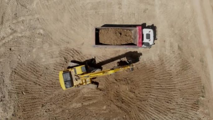 施工现场工业挖掘机装载地面进入自卸车的4k俯视图。
