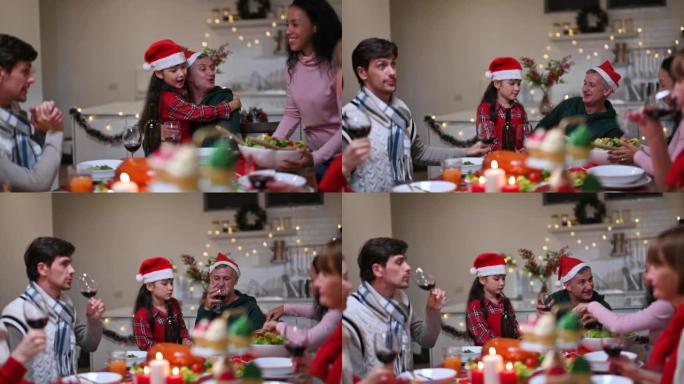 快乐的多元化家庭拥抱，并在他们家中的餐桌上品尝美食和美酒庆祝圣诞节，当沙拉被带上并举起眼镜时。
