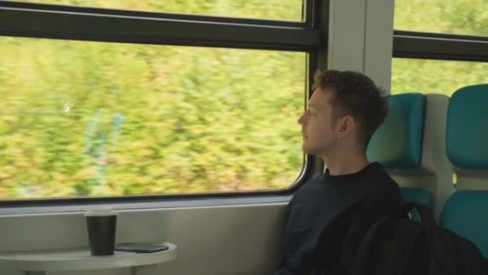 年轻英俊的白人男子坐在窗边享受火车旅行，看着外面的大自然