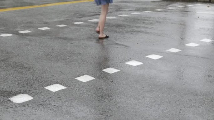 白天在城市穿越线路上倾盆大雨，行人横穿马路。选择性地关注有雨滴的柏油路。