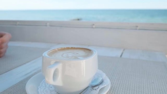 在海滩上的人行道咖啡馆的桌子上，一杯带有泡沫的卡布奇诺咖啡。特写