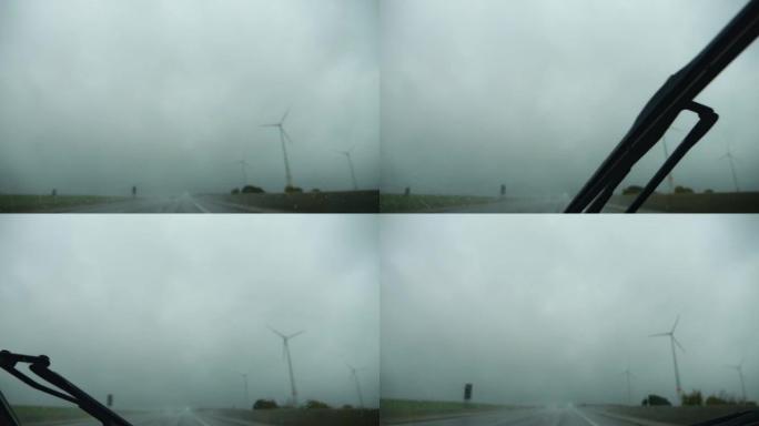 在雨中，在阴沉的天气里，在高速公路上行驶。雨刮器擦拭汽车雨水浸湿的挡风玻璃。可见风力涡轮机。版本6