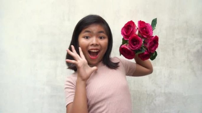 亚洲少女手持一束粉红色的花朵，摆姿势吹一个吻，惊喜，哇!，敬畏的手势，白色的旧墙背景