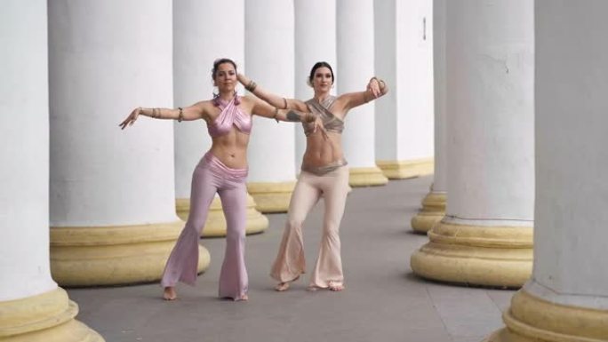 两名才华横溢的舞者同时摇动身体在户外表演印度舞蹈。苗条灵活的女人在城市的白色柱子之间弯曲跳舞。