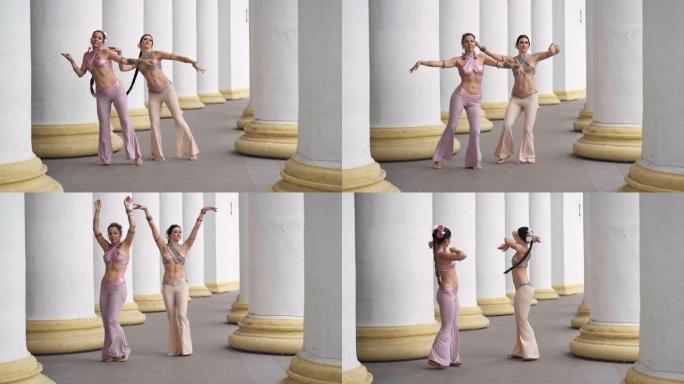 两名才华横溢的舞者同时摇动身体在户外表演印度舞蹈。苗条灵活的女人在城市的白色柱子之间弯曲跳舞。