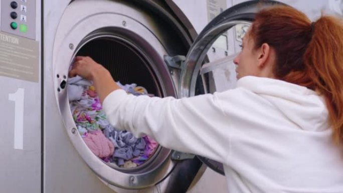 家庭主妇年轻女子做家务，忙于常规的家务工作，把毛巾放进洗衣机，在舒适的洗衣房里打开现代洗衣机烘干机。
