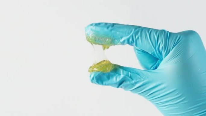 工人用两根手指挤压锂润滑脂，并在实验室中看到隔离在白色背景上的润滑脂纤维。手指上的黄色透明油脂。测试