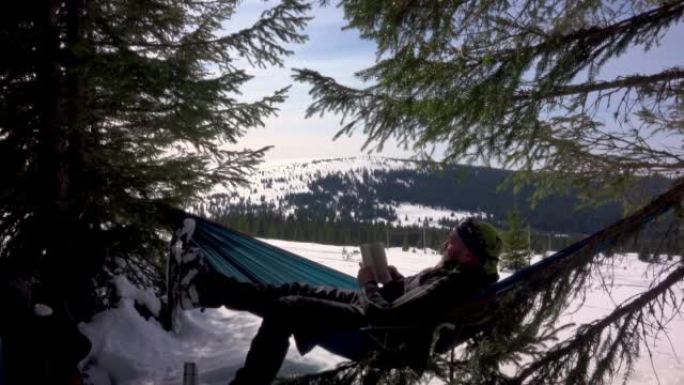 徒步旅行者放松和看书，躺在冬季森林的吊床上