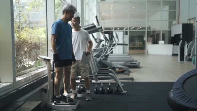 亚洲中国健身教练在健身房测量老年人身高和体重