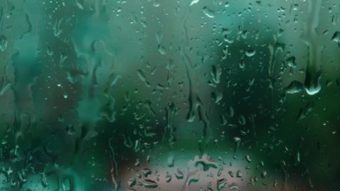 从窗口观看。雨滴在深绿色背景下的玻璃上模糊。实时视频。