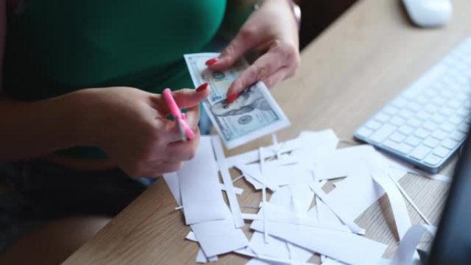 女造假者在工作桌上用剪刀剪下美元钞票