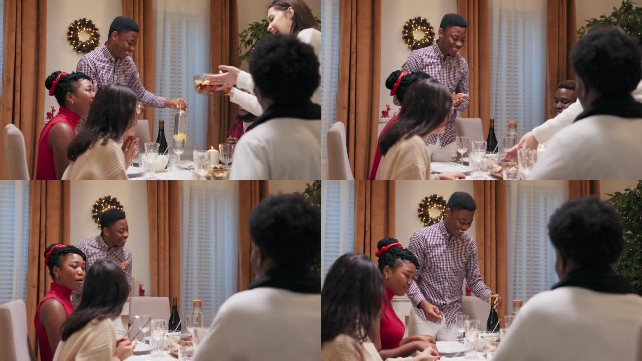 圣诞节前夕，朋友们聚集在节日的餐桌旁。他们吃饭、喝酒和社交。非洲人的外表站在餐桌旁，提供葡萄酒。女人