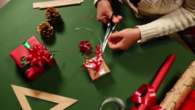 女人的手的俯视图使用剪刀，在绑好圣诞节礼物的同时将白色装饰带切成条状