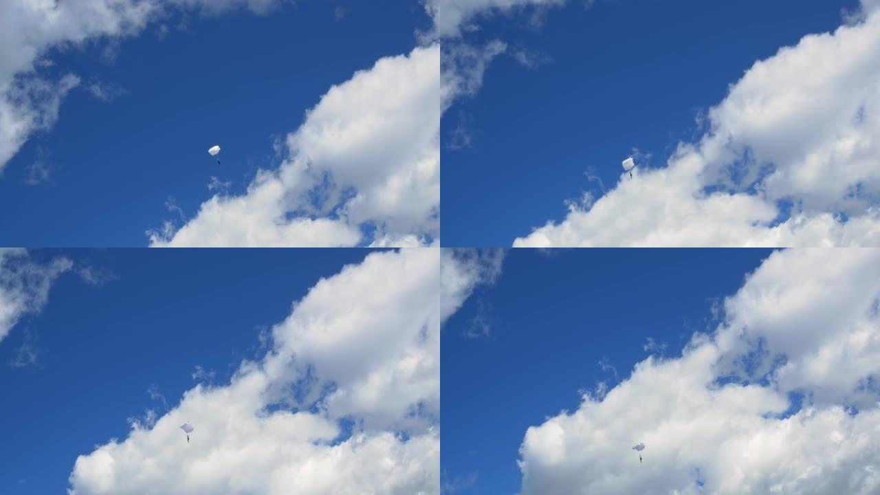 白色降落伞上的跳伞运动员在美丽的白云之间的空中滑行。无畏的跳伞者通过在机翼式降落伞上像高高的飞鸟一样