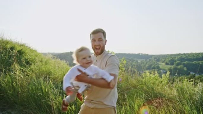 快乐而自豪的年轻父亲抱着他的笑意婴儿在户外的户外，阳光照耀着他的手臂
