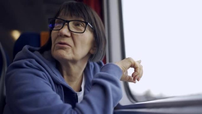 一位戴着眼镜的老妇乘火车坐在窗户附近，与邻居交谈。