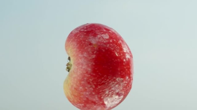 半个红苹果在蓝天背景下旋转，特写。
