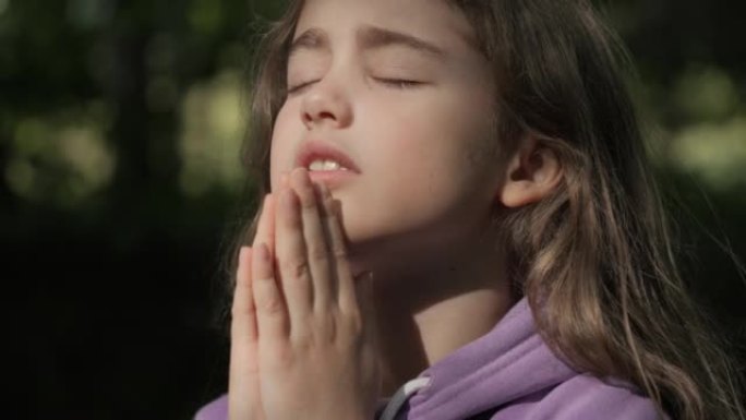 宗教。小女孩在户外祈祷时双手合十，向上帝祈祷。忧心忡忡的少女寻找希望和信仰向上帝祈祷。心中充满希望的