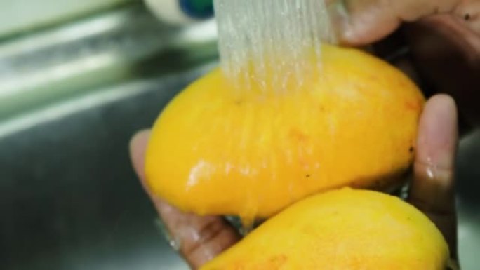 关闭男人手在家里的自来水下洗芒果型Kepodang