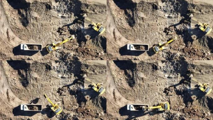 工业矿山挖掘机正在挖掘施工现场的土壤并装载卡车。空中无人机俯视图。