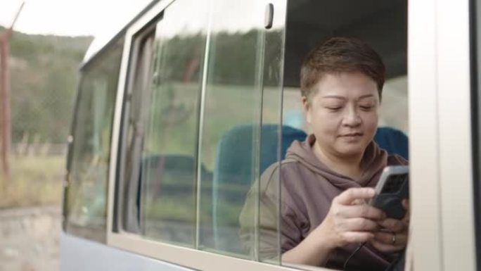使用智能手机坐在公交车上的亚洲华裔妇女
