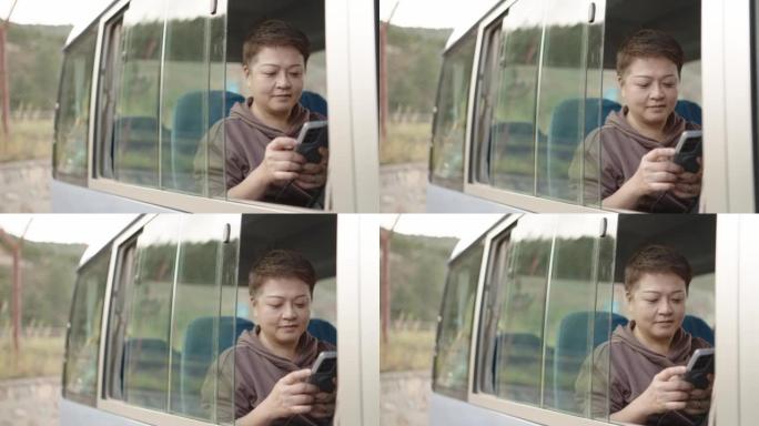 使用智能手机坐在公交车上的亚洲华裔妇女