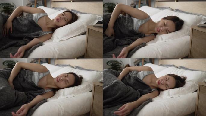 侧视亚洲妇女躺在白色床单上胃痛。生病的女士在家里舒适的地方睡觉时抱着痛苦的肚子。患病女性在卧室里腹部