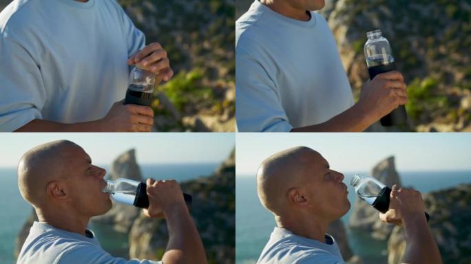 运动员男子在海洋悬崖特写处喝瓶装水。合适的家伙打开水壶