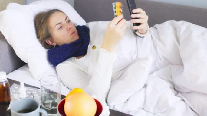 患有重感冒，流感或冠状病毒的患病年轻女子发热拿着药物，同时通过智能手机通过视频链接咨询医生。生病的妇