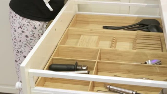厨柜开放式抽屉，带餐具隔间，女人把叉子勺子放在竹木餐具收纳器里。餐具储物托盘特写。