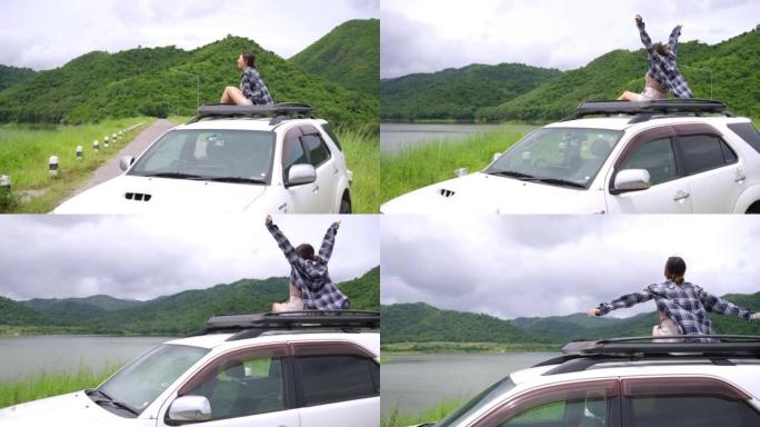 4k亚洲妇女坐在车顶行李架上，举起手臂，在暑假公路旅行中旅行。