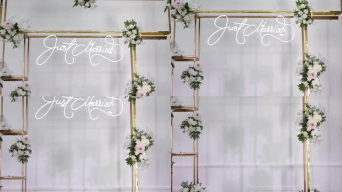 美丽的金色金属婚礼拱门装饰着新鲜的白花和绿色，背景上有白布。婚礼派对庆典。