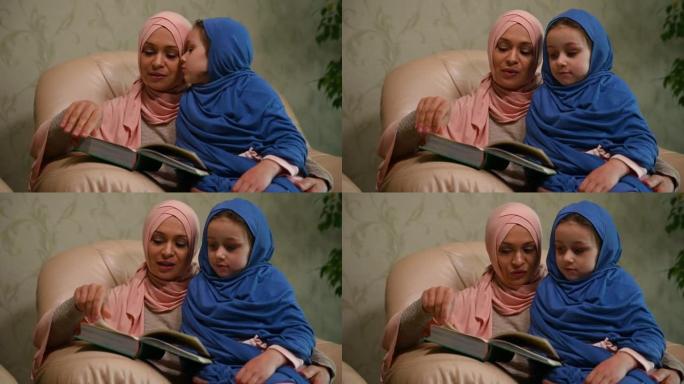 穿着粉红色头巾的穆斯林爱心妈妈为她的小女儿读了一本书，拥抱着她坐在现代客厅的沙发上