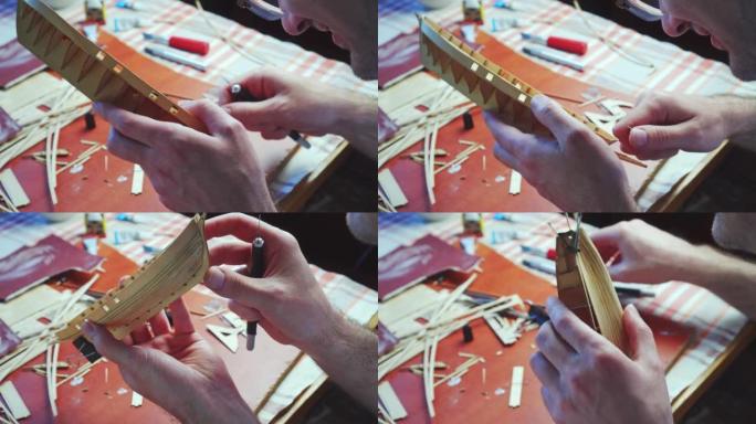 人的手用胶合板上的文书刀切出船模的细节。建造玩具船、爱好和手工艺品的过程。工作台有各种材料、零件和工