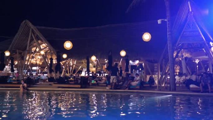 在酒店的游泳池旁为成年人拍摄的晚会，音乐响亮，聚光灯明亮。为想要以最快速度放松的度假酒店游客举办的派