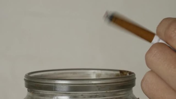 一只拿着香烟的手将骨灰倒入烟灰缸中