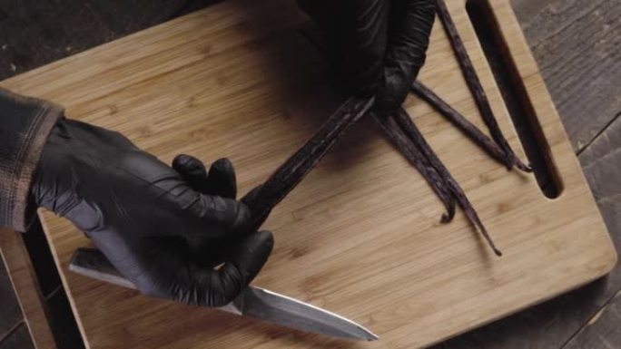 男性戴着丁腈手套的俯视图，在切菜板上显示香草豆荚种子的内部