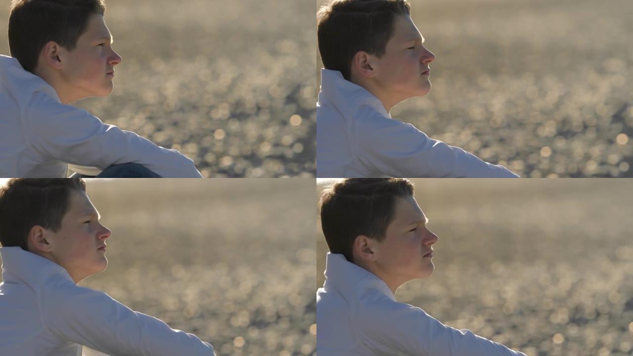 思想，关心-坐在海边的沉思男孩在阳光明媚的日子里叹息思考