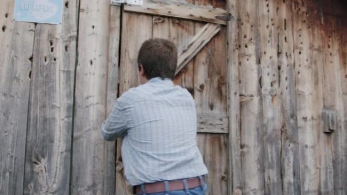 年轻的农民男孩在美国科罗拉多州一个小镇的家庭牧场上关闭并锁住了木制鸡舍或外部存储棚的门