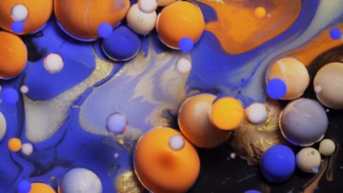 彩色的蓝色橙色和白色气泡散布在宇宙色彩表面，并混合在抽象设计中。金色闪闪发光的颗粒，墨球滴并在液体中