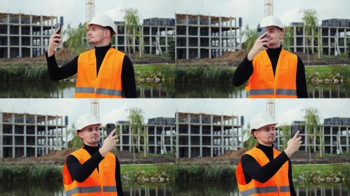 戴着白色安全帽的年轻迷人工程师用手机拍摄在建建筑的照片。男性通过智能手机向客户发送消息。工程项目。