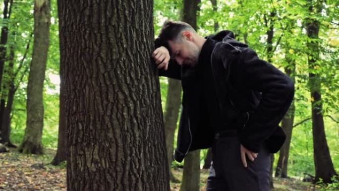 沮丧的男性脸悲伤的压力男人站在户外森林的树附近，抱着头，因为深深的沮丧而哭泣，冒犯了面部表情担心麻烦
