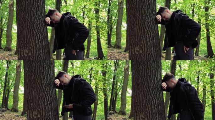沮丧的男性脸悲伤的压力男人站在户外森林的树附近，抱着头，因为深深的沮丧而哭泣，冒犯了面部表情担心麻烦