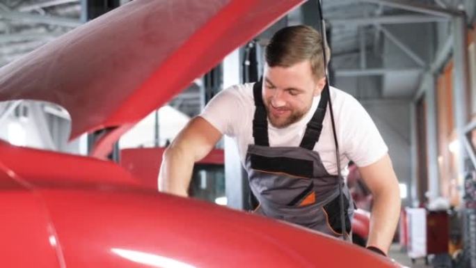 一位年轻的大胡子汽车修理工在车库的引擎盖下检查汽车。