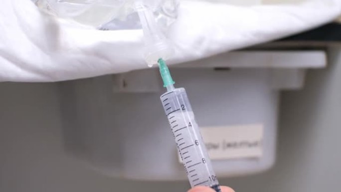 医生用注射器针头用溶液刺穿玻璃卷中的软木塞，并抽出一剂药物。医生为生病的病人准备注射药物。