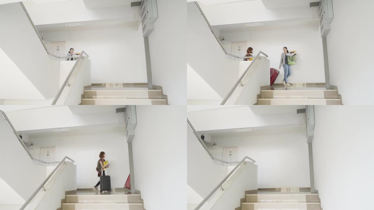 两个亚洲妇女提着她们的行李从楼梯走到宿舍走廊。