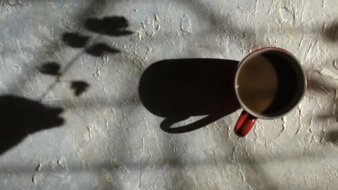 模糊的阴影女性手与花的垃圾背景与咖啡杯。高对比度。抽象，光影的游戏