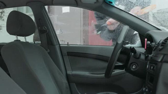 车主将汽车前门的窗户从雪地上清洗干净。