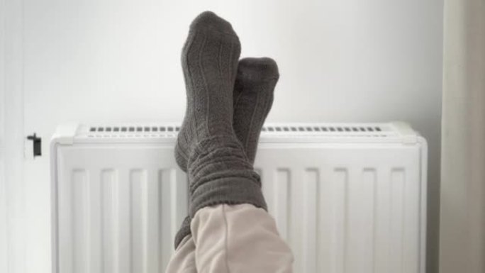 一名妇女在家用取暖器散热器上穿着羊毛保暖袜给冷冻的脚加热